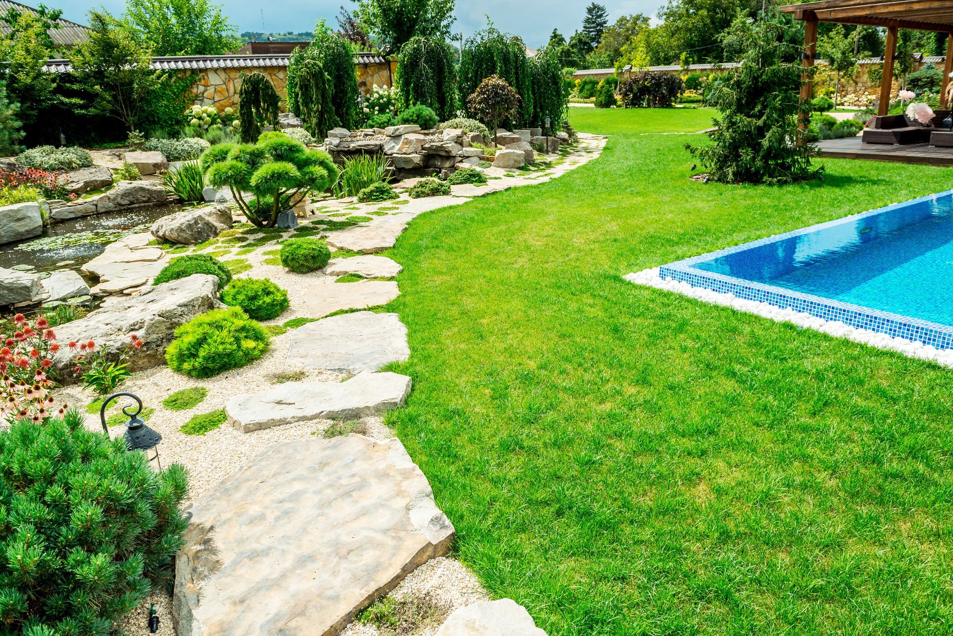 Landscaped backyard with stone path, lush green lawn, rock garden, and blue swimming pool
