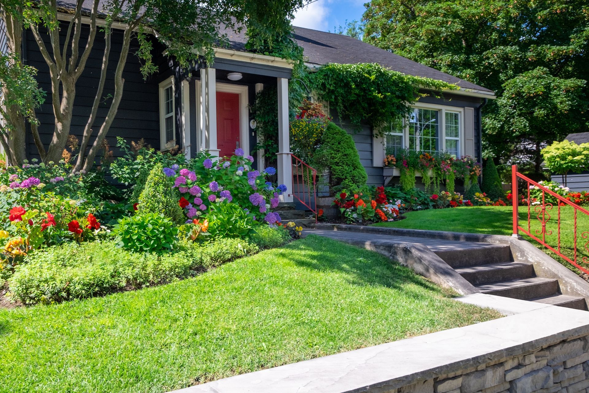 Suburban house with lush flower garden, green lawn, and stone steps by a front walkway