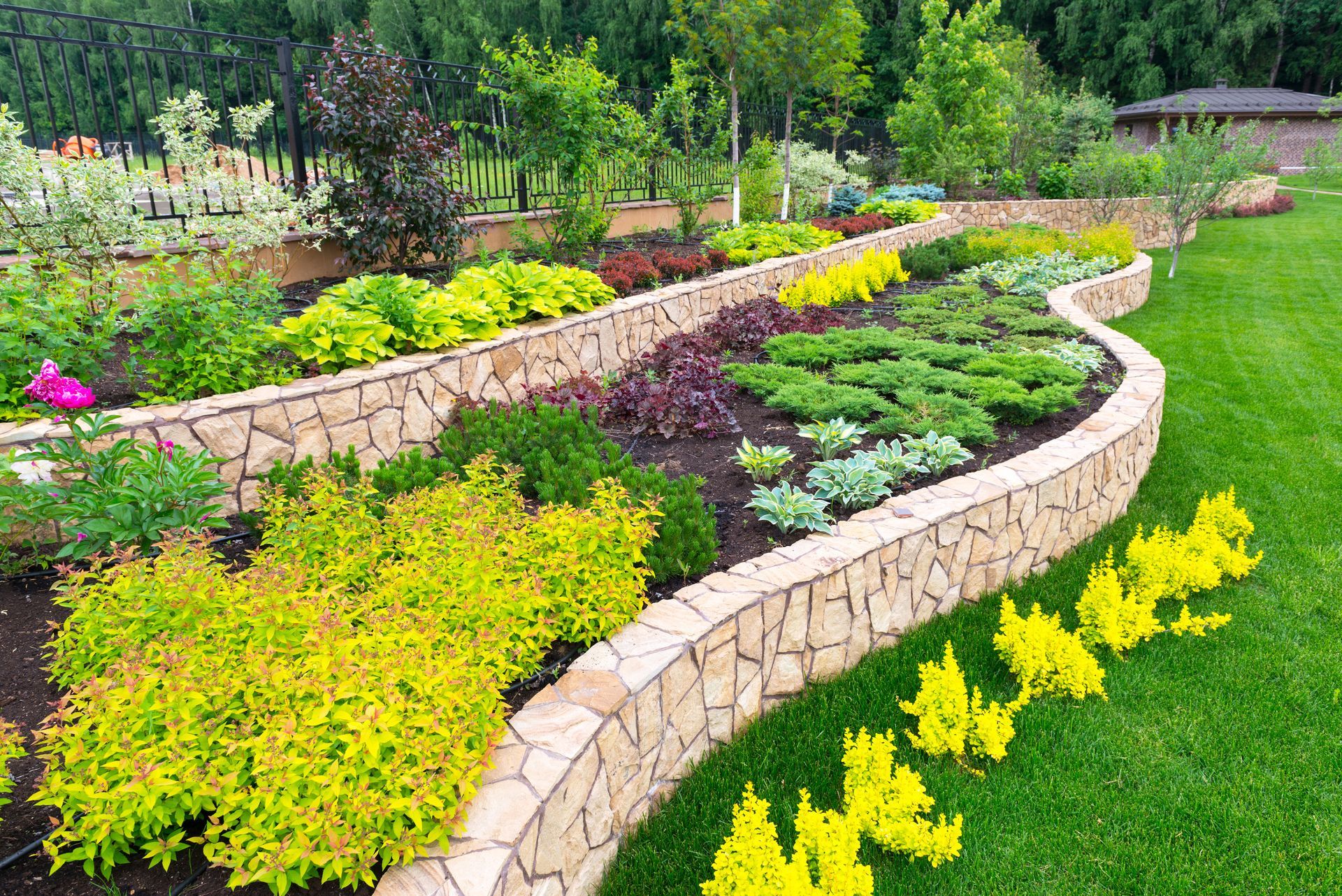 Curved stone garden beds with colorful flowers and shrubs along a green lawn