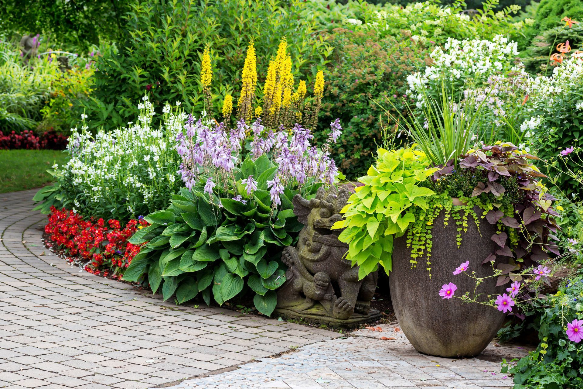 Colorful flower bed and potted plants beside a stone path in a lush garden