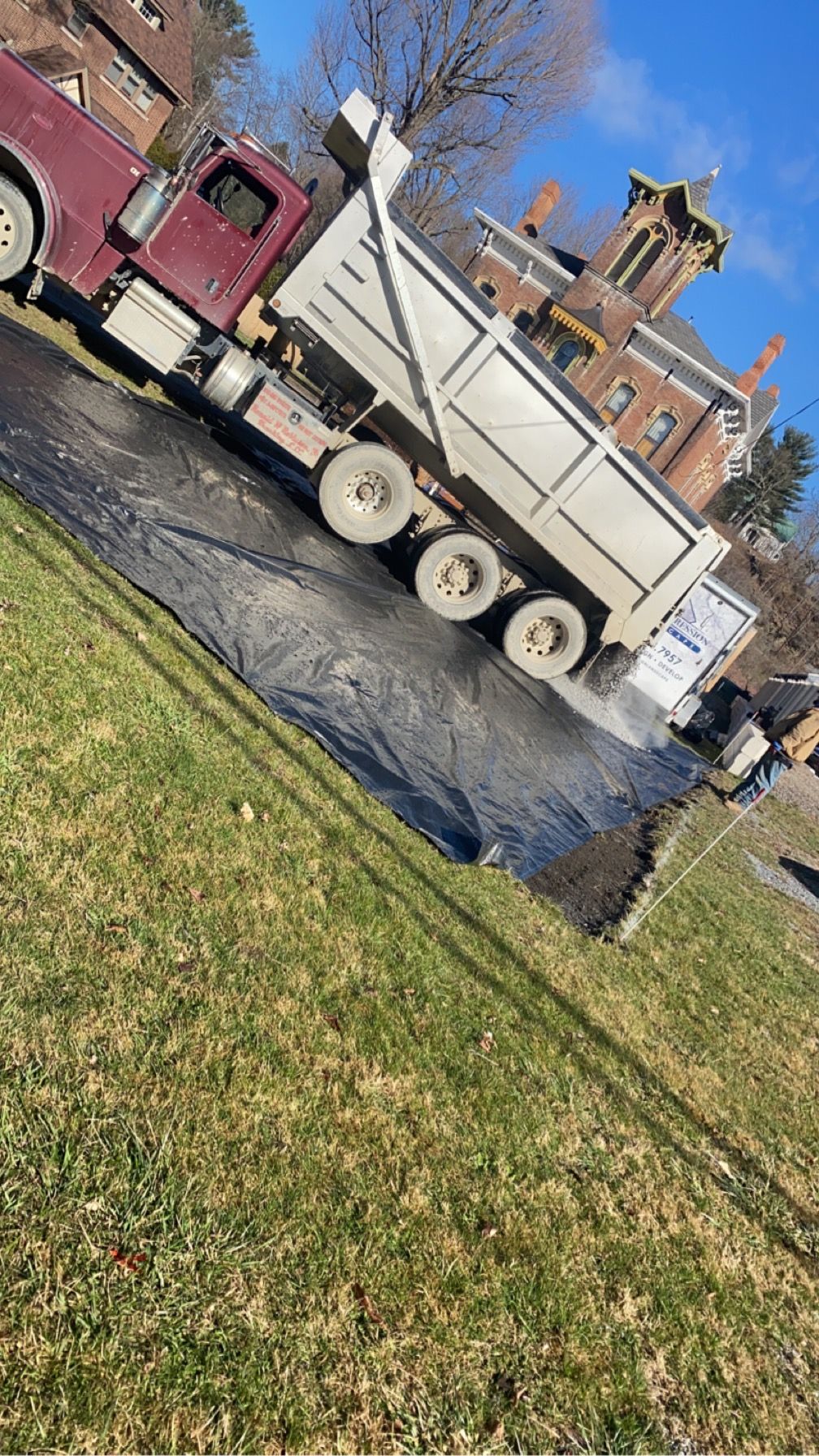 Dump truck unloading black asphalt on a sloped residential street beside a lawn.
