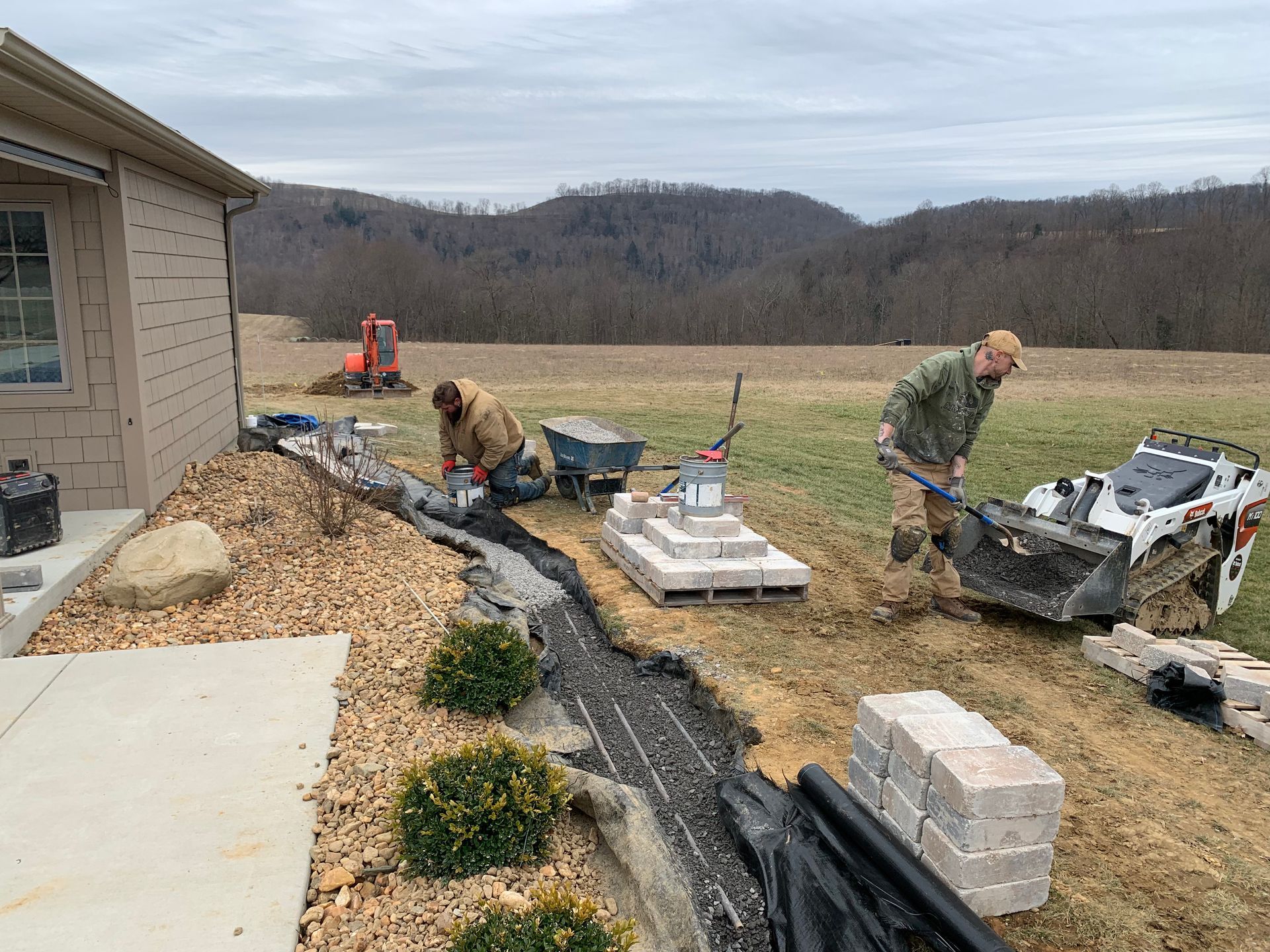 Workers installing a stone walkway beside a house in a rural yard