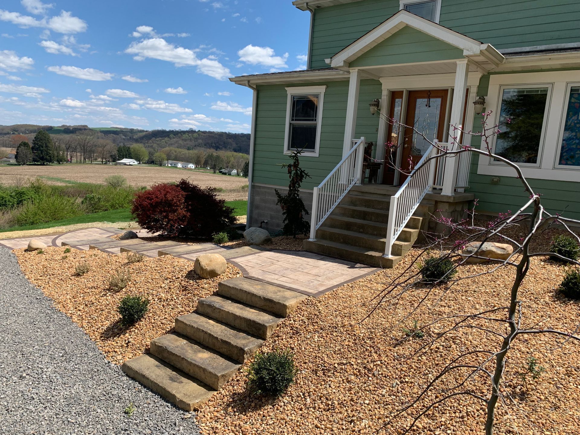Green house with front steps, gravel path, and landscaped yard under a blue sky