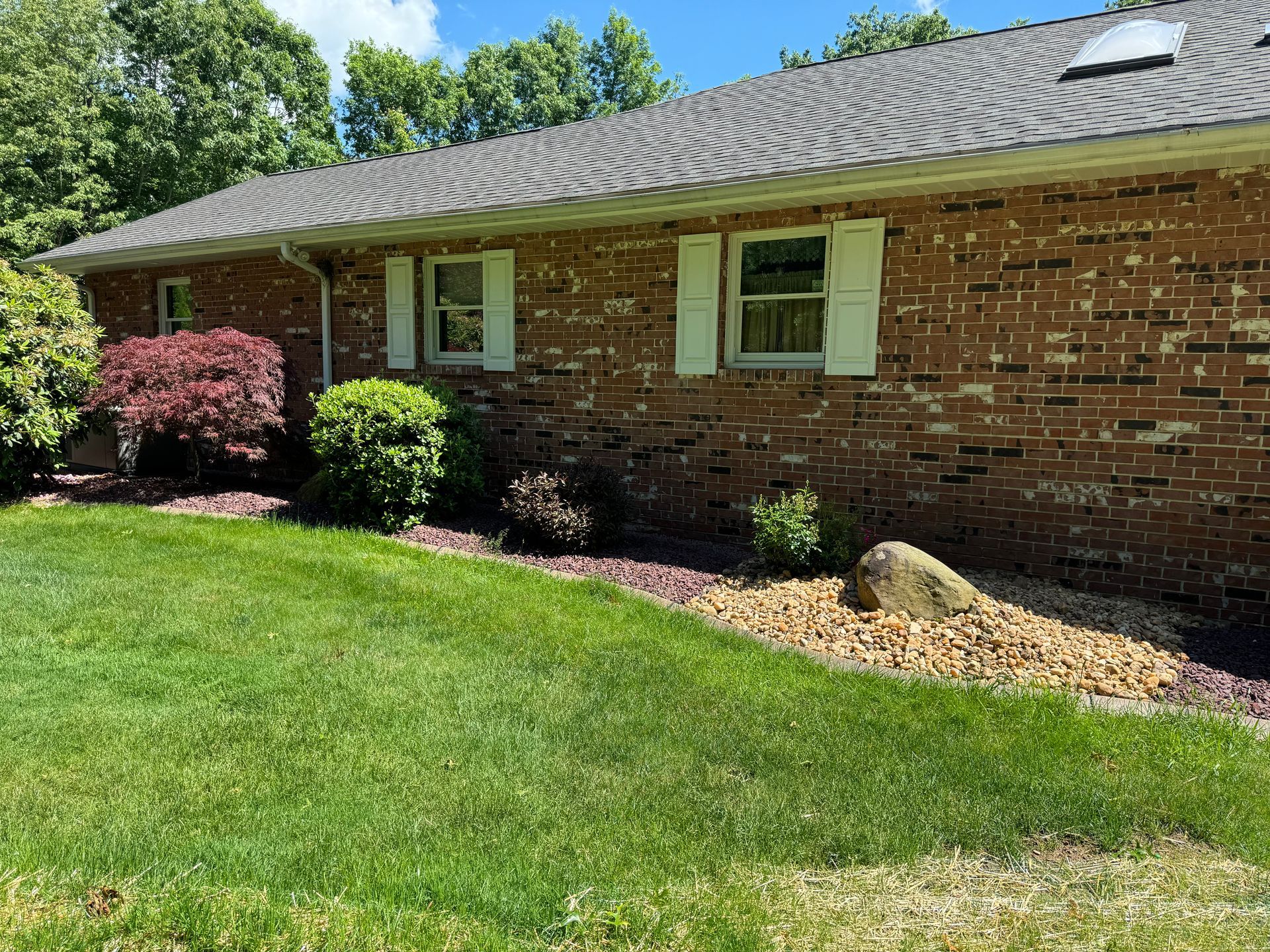 Brick house exterior with white shutters, green lawn, and landscaped shrubs under a blue sky