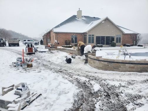 Snow-covered suburban house under construction with workers and equipment on a muddy driveway