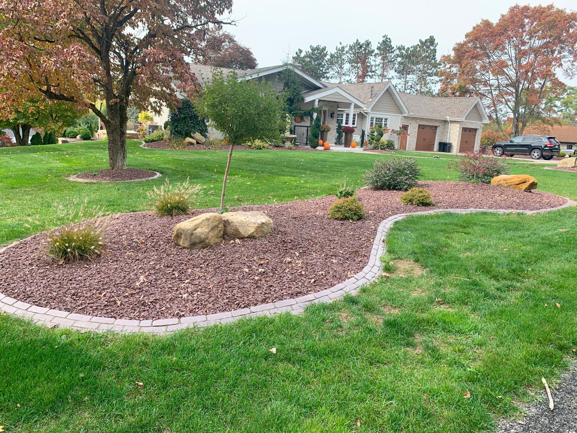 Curved mulch garden bed with shrubs and rocks in a green front yard, with a house in the background
