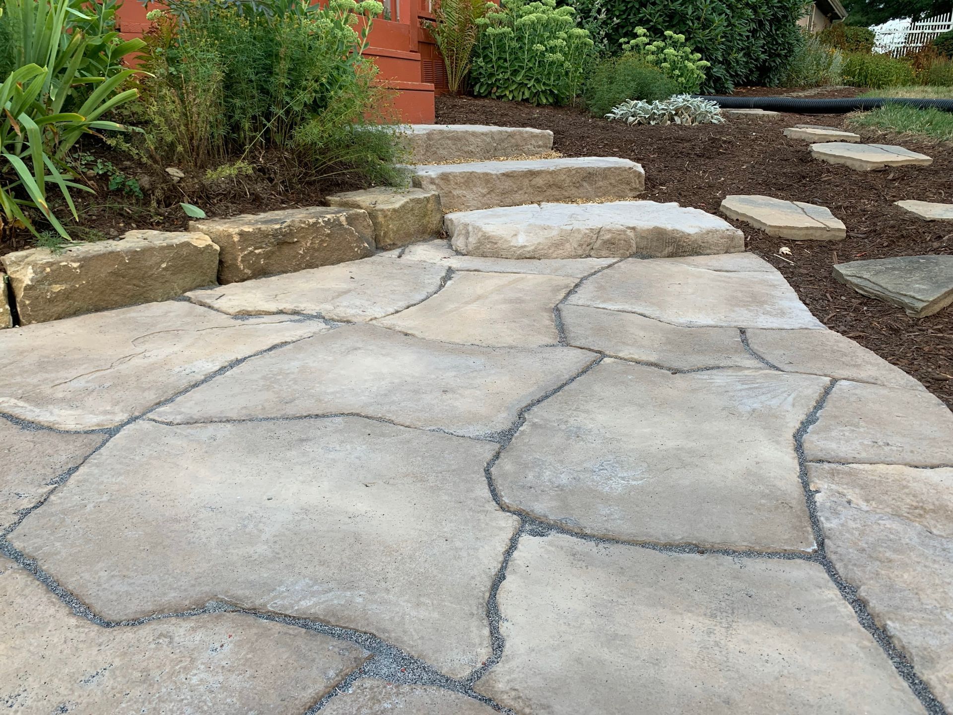 Stone garden path with irregular pavers leading up steps beside plants and mulch