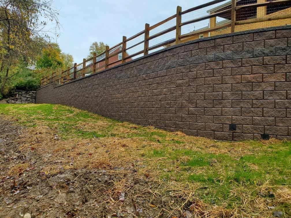 Stone retaining wall beside a grassy slope with a wooden fence on top under cloudy skies