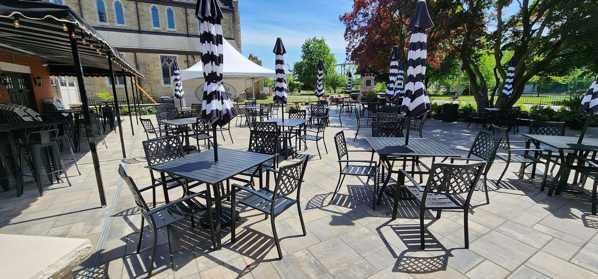 Outdoor café patio with black metal tables and chairs under striped umbrellas on a sunny day