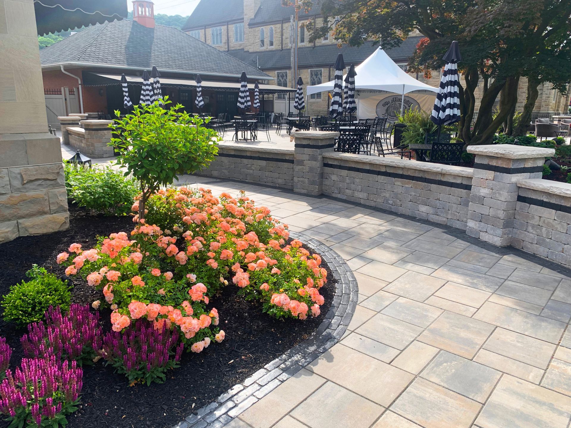 Flower garden beside a stone patio with pink and orange blooms in a sunny courtyard