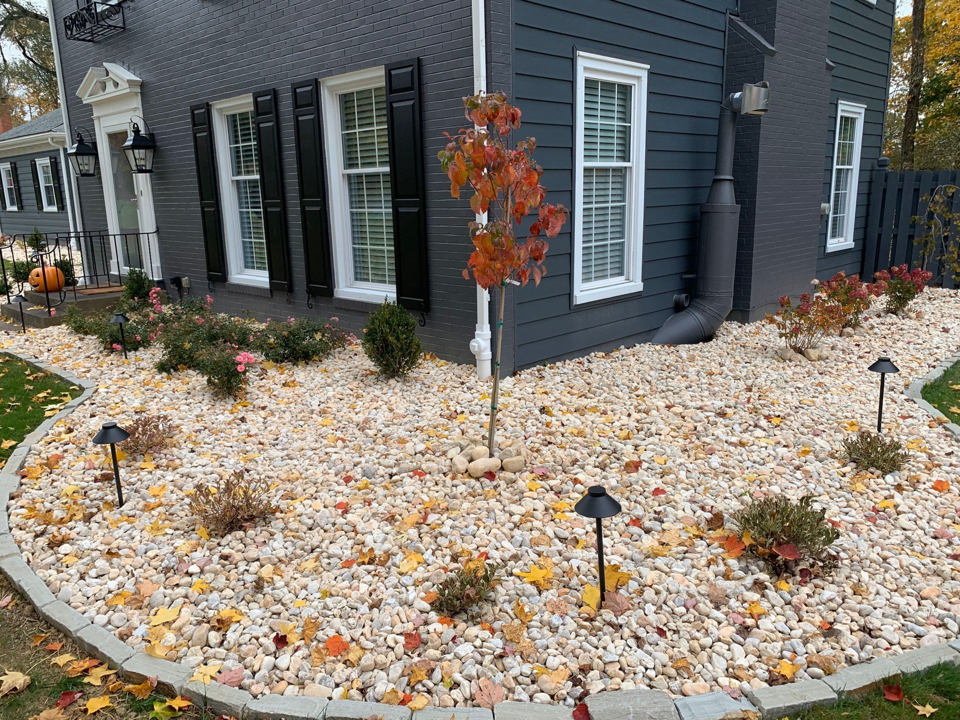 Dark gray house with black shutters and a rock garden with small plants and lights