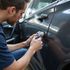 Man using a tool to manipulate a car door lock on a dark gray vehicle.