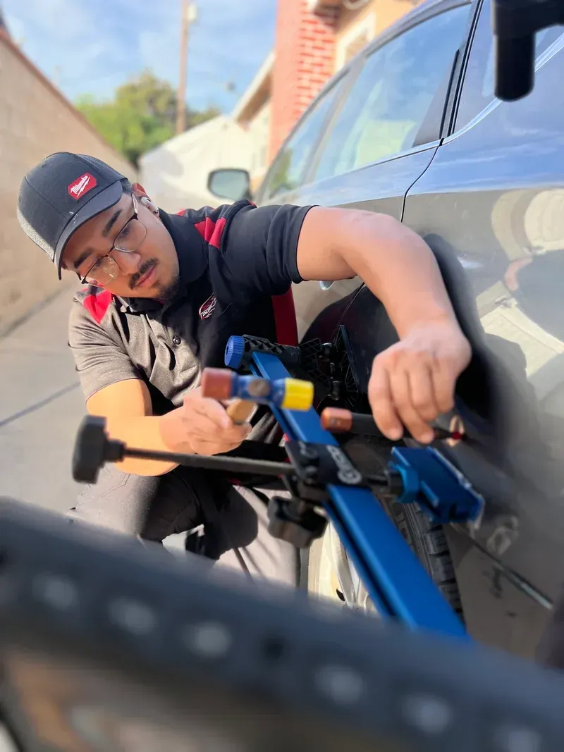Mechanic using a tool to work on a gray car door in a garage.