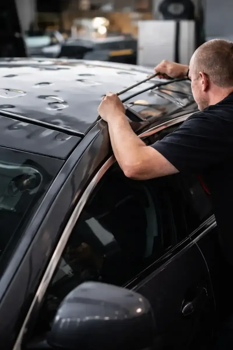 Technician working on hail-damaged vehicle roof using paintless dent repair tools