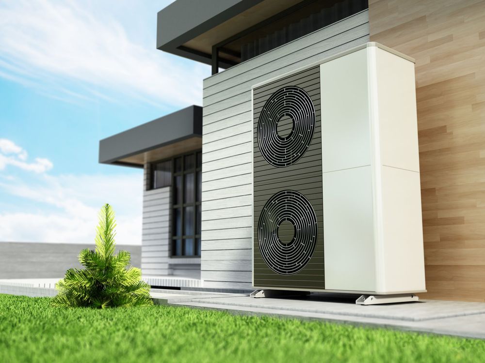 Unità di pompa di calore ad aria accanto a una casa moderna in una giornata di sole.