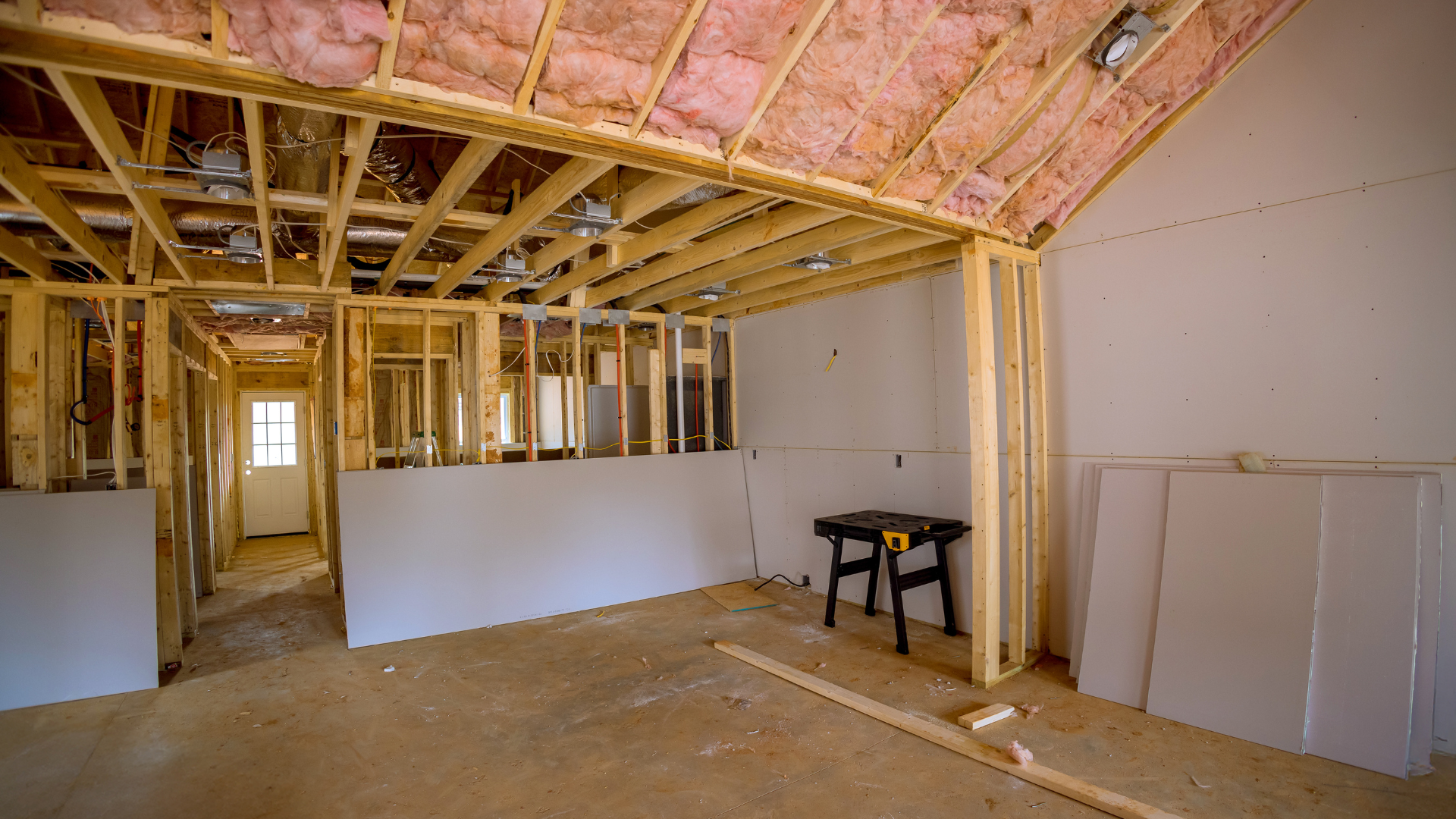 Unfinished room under renovation with exposed wood framing, pink insulation, and drywall panels.
