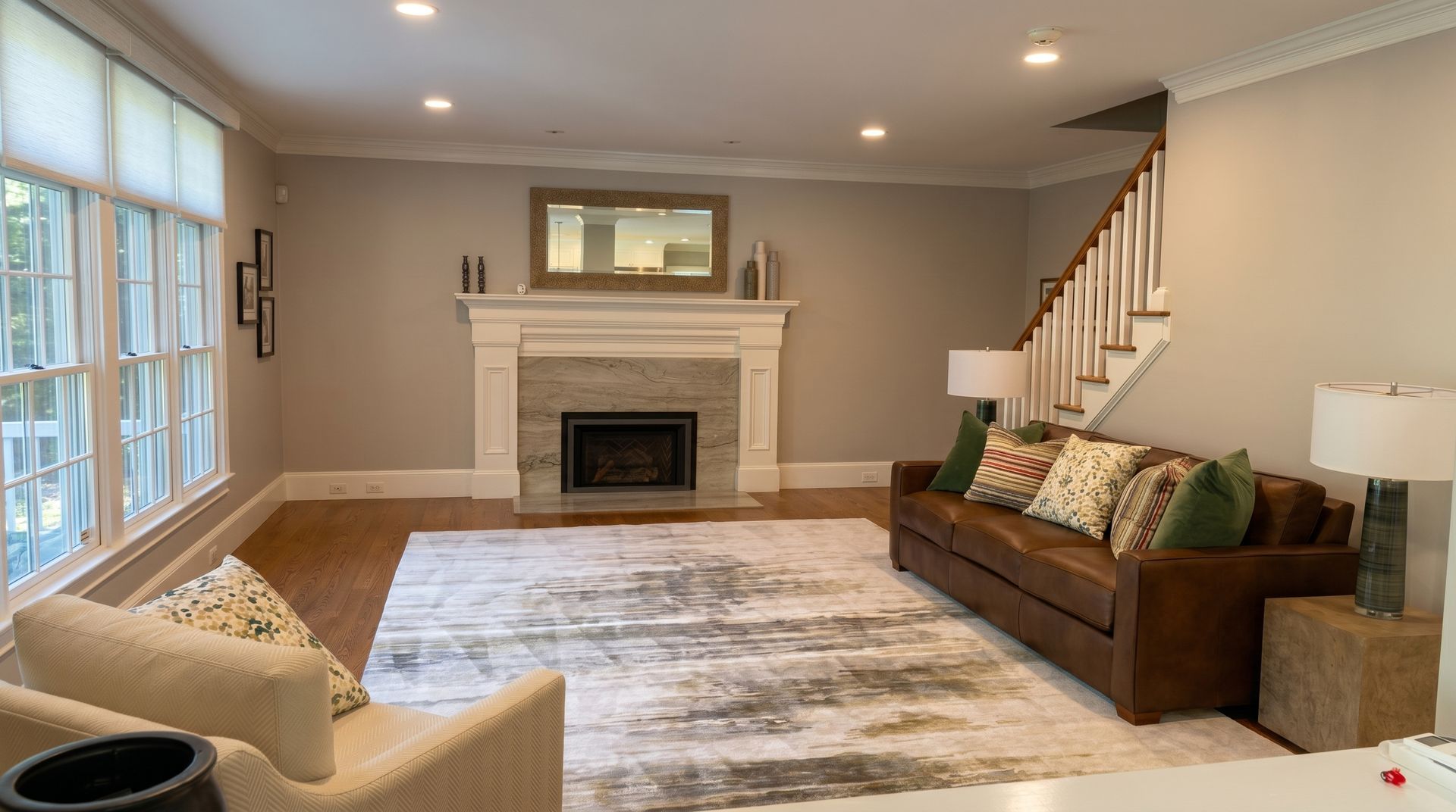 Bright living room with fireplace, beige walls, sofa, armchair, staircase, and large area rug.