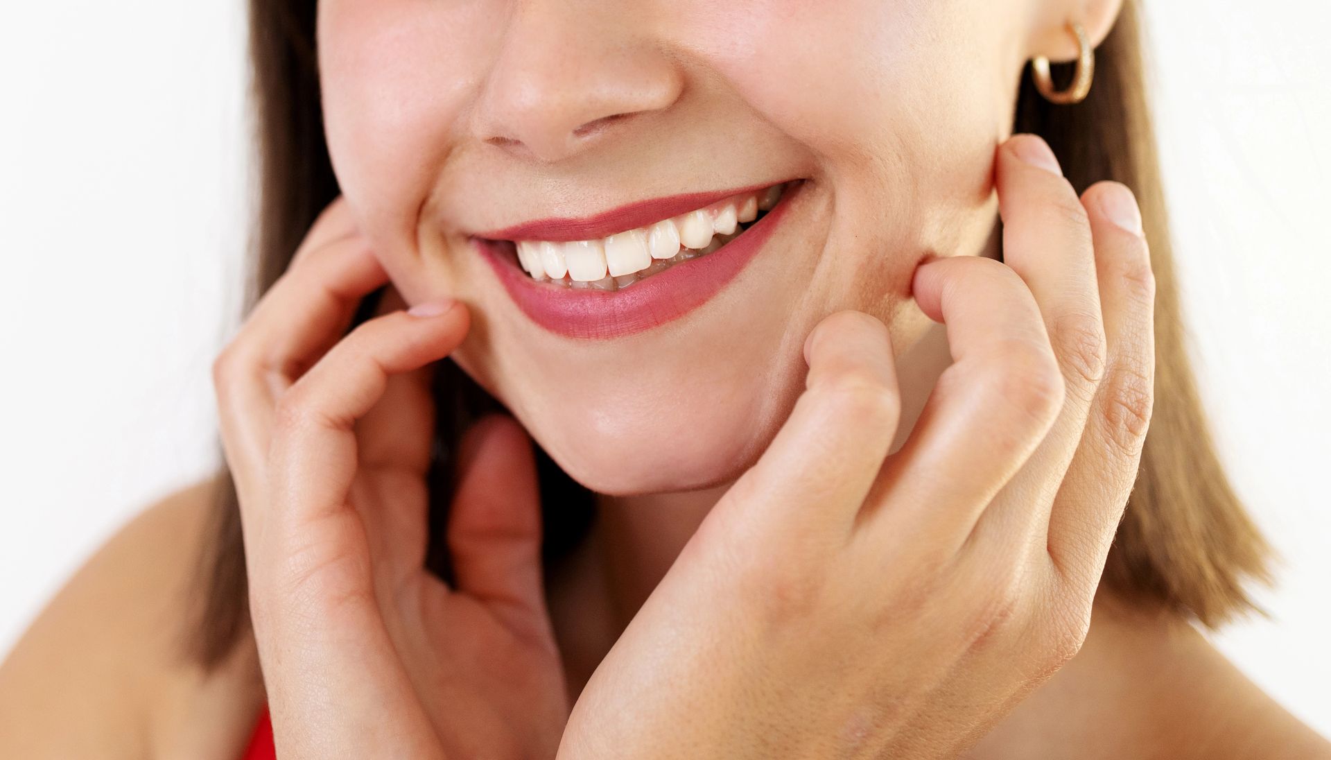 Primo piano di una persona sorridente con le mani che sfiorano delicatamente i lati del viso.