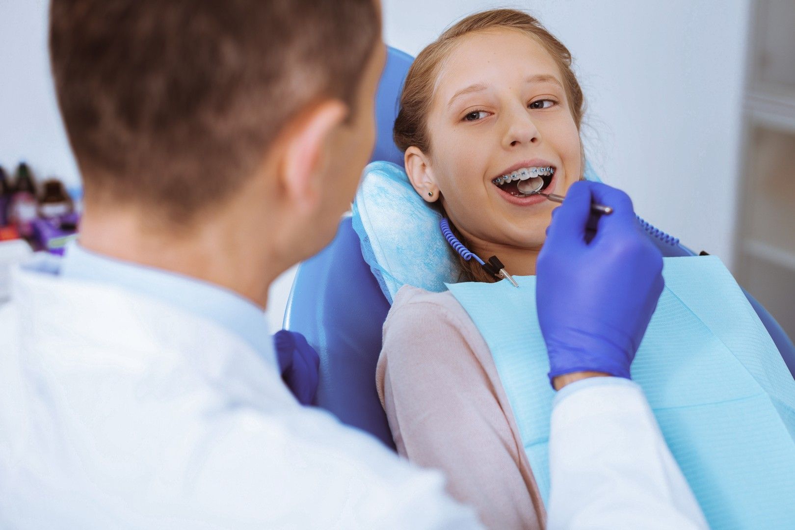 Un dentista in camice bianco esamina i denti di un paziente seduto su una poltrona con l'apparecchio ortodontico.
