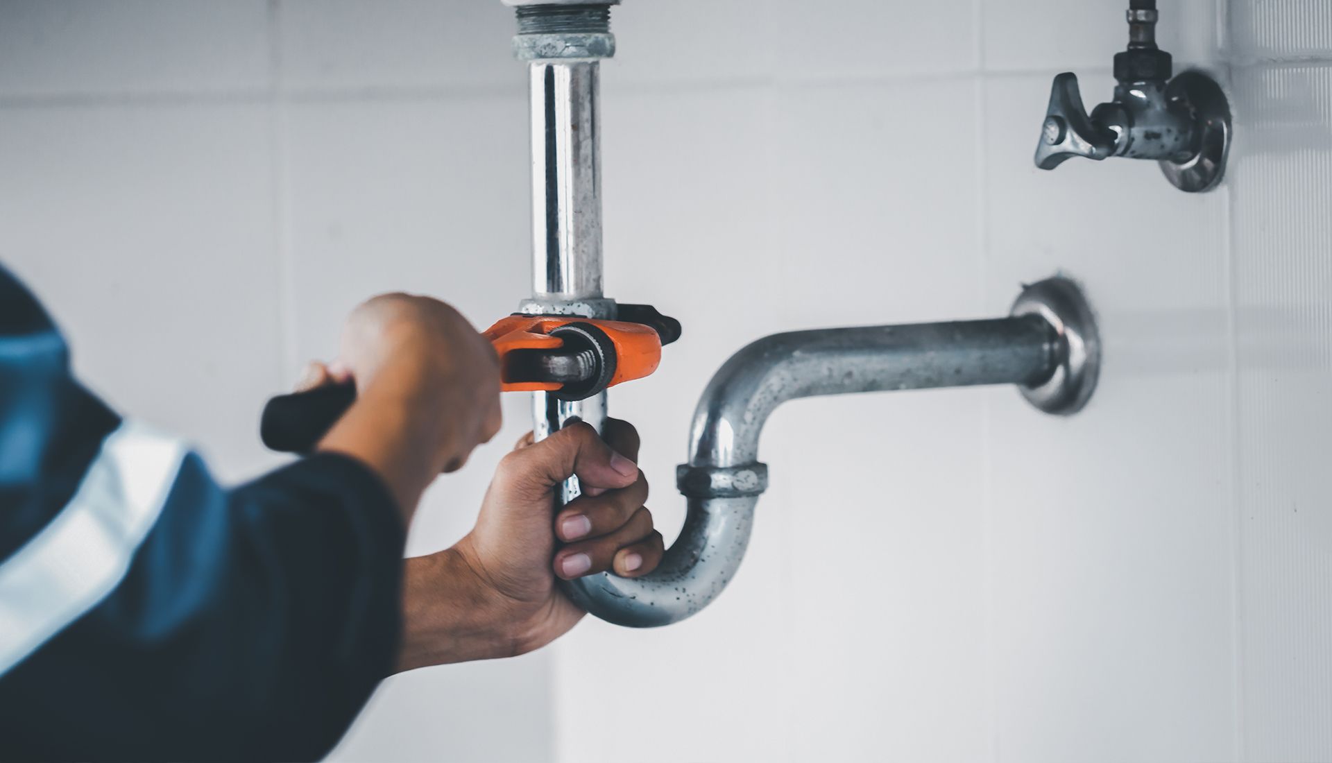 A plumber is fixing a pipe with a wrench in a bathroom.