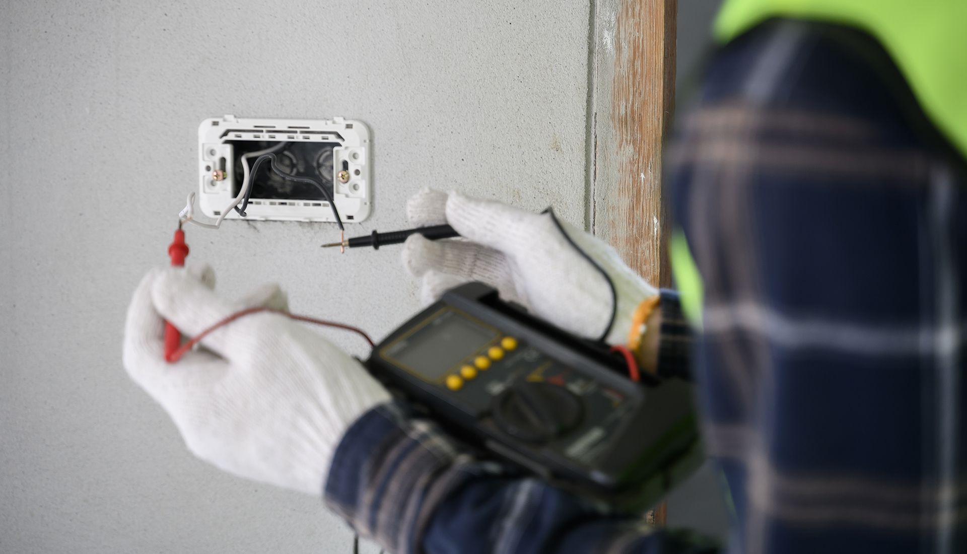 An electrician is using a multimeter to test an electrical outlet.
