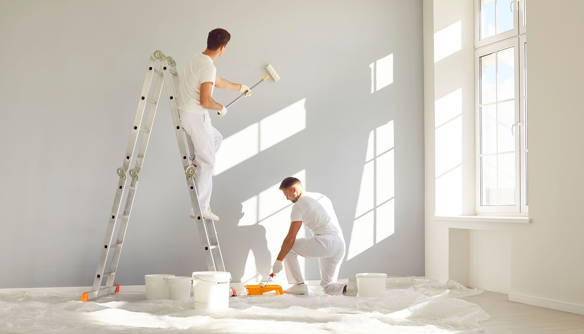 Two men are painting a wall in a room.