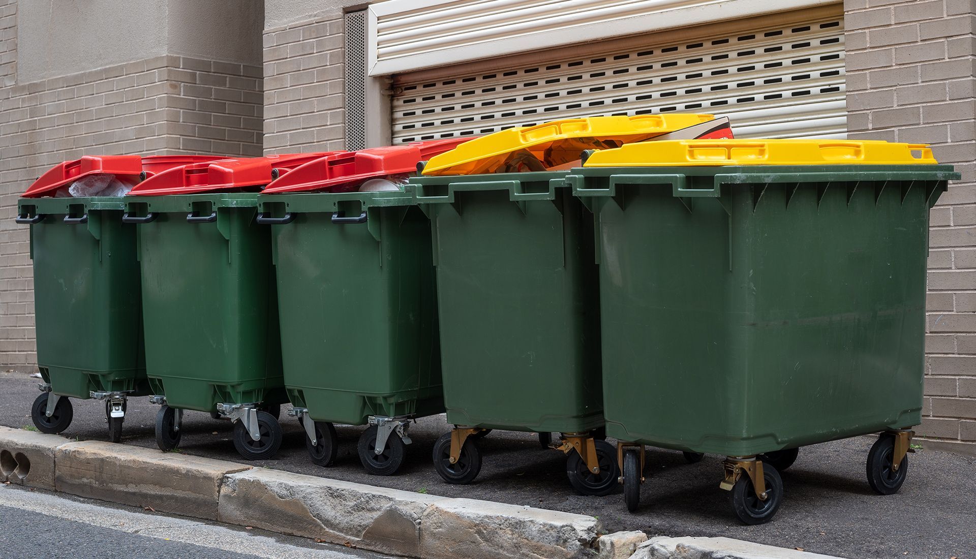 A row of garbage cans are lined up on the side of the road.