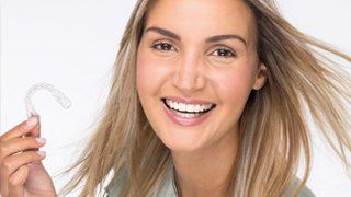 Lächelnde Frau, hält durchsichtigen Invisalign-Aligner, weißer Hintergrund.