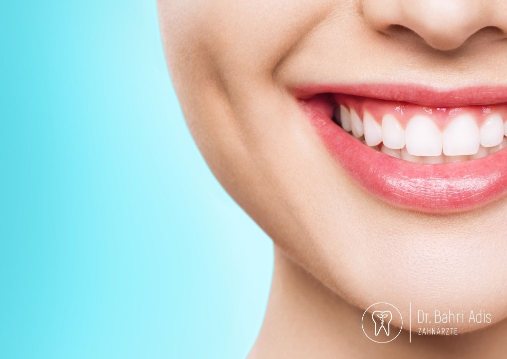 Nahaufnahme des strahlenden Lächelns einer Frau mit weißen Zähnen und rosa Lippen vor blauem Hintergrund.