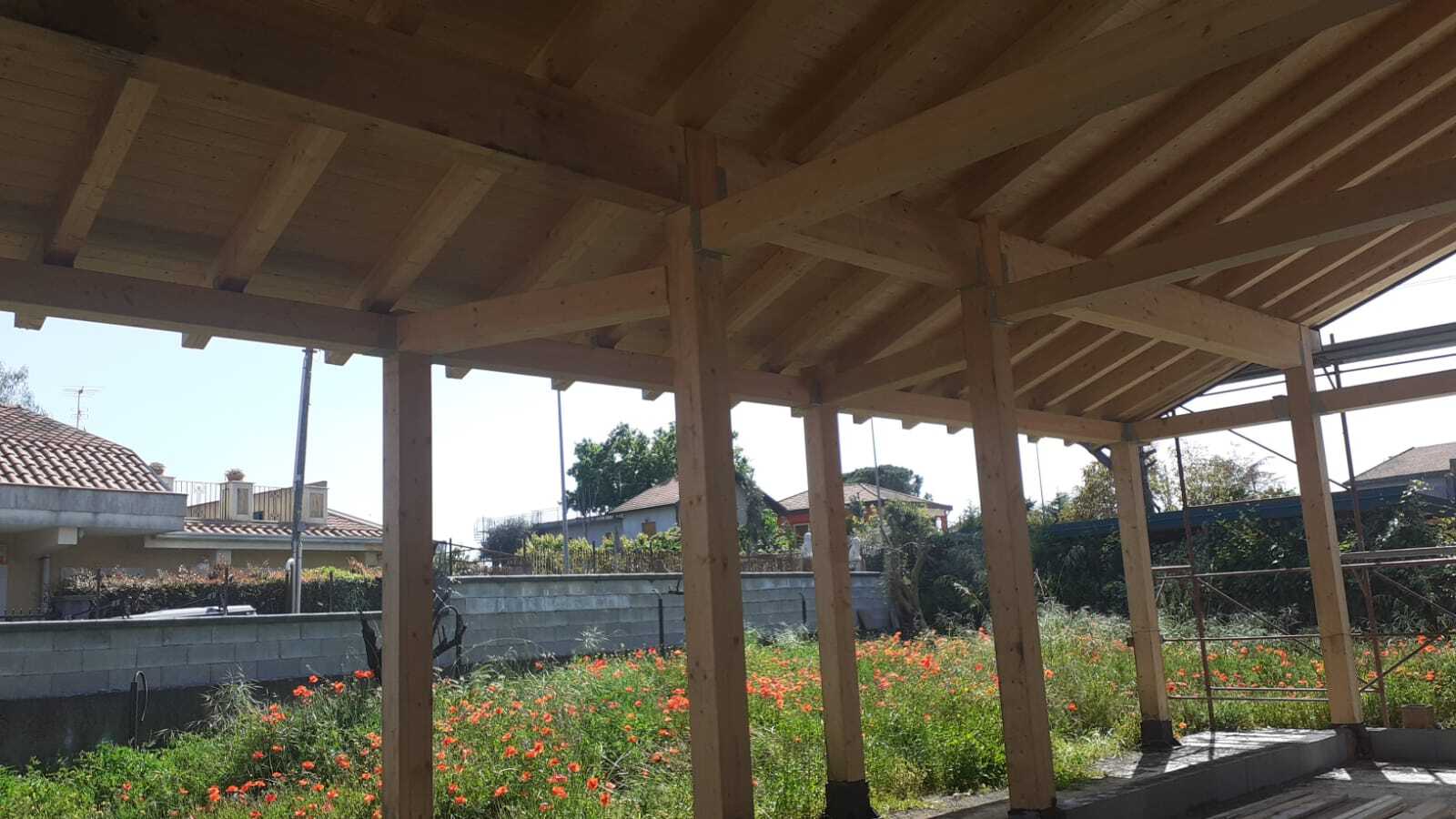 Pergola in legno con colonne di sostegno sopra un giardino. Si vede il cielo.