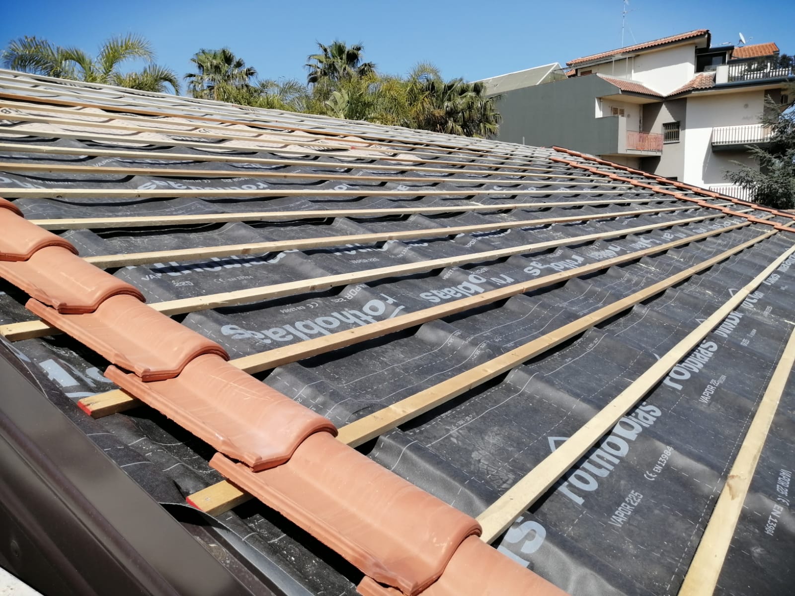 Tetto in costruzione con tegole rosse, travi in legno e sottofondo nero.