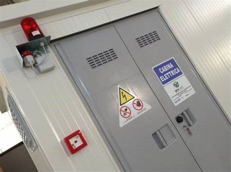 Armadio elettrico grigio con etichette di avvertenza, una luce rossa di emergenza e un pulsante.
