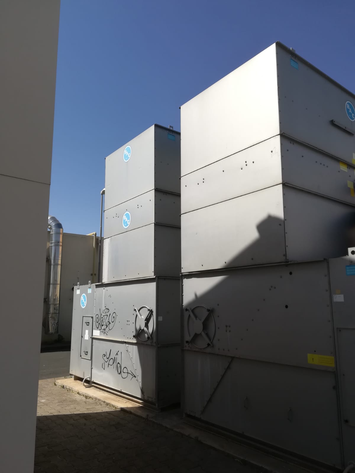 Unità HVAC grigie impilate su un tetto contro un cielo azzurro e terso.