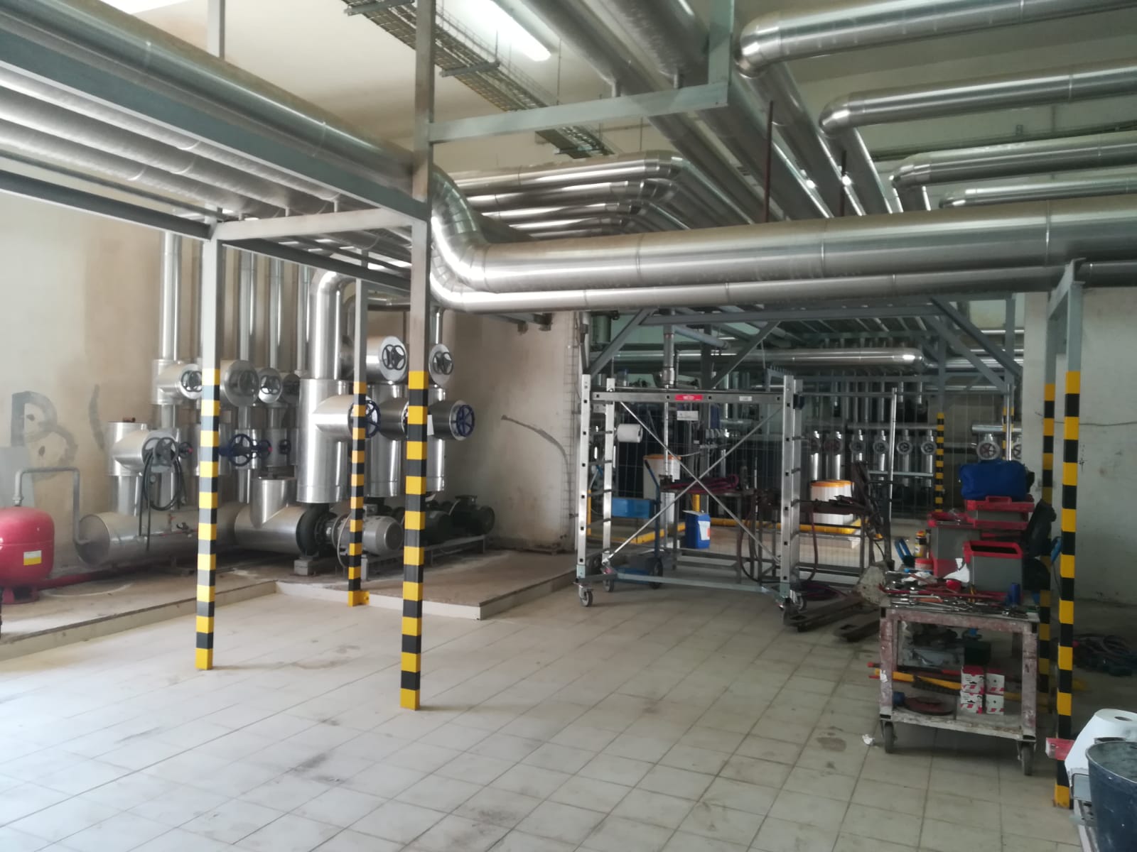 Spazio industriale con tubi in acciaio, isolamento e impalcature in costruzione.