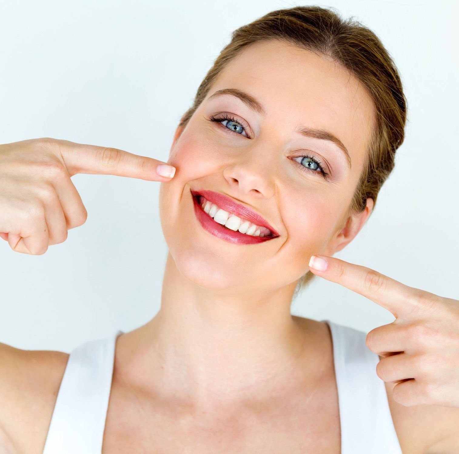 Woman smiling, pointing to her cheeks, showing off teeth.