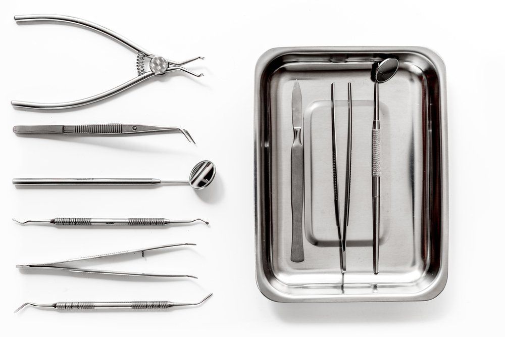 Instruments dentaires disposés sur une surface blanche, notamment des forceps, un miroir et un plateau d'instruments.