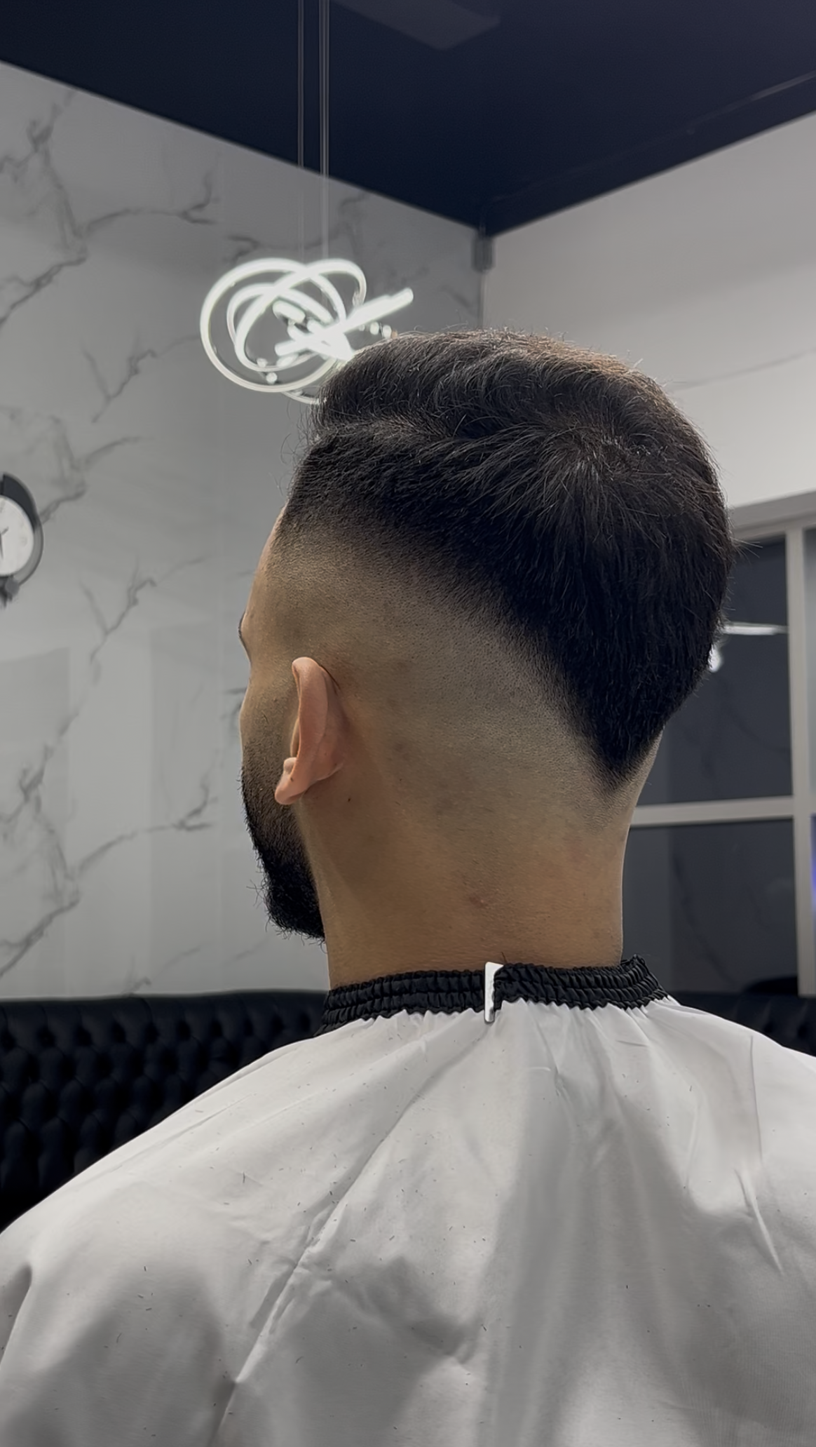 Person with a faded haircut at the barber shop. The hair is dark on top and faded to the skin.