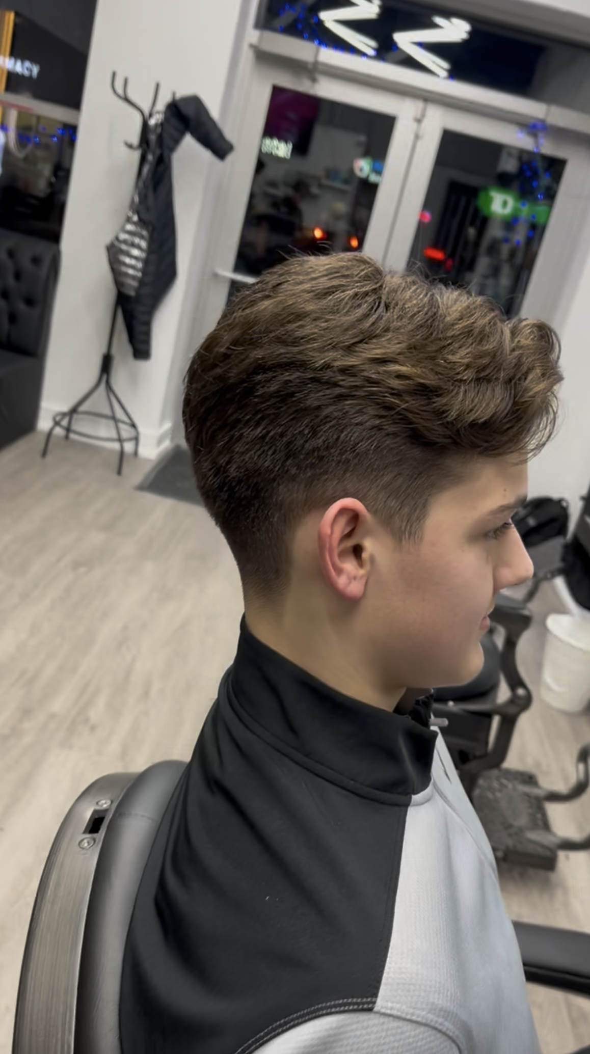 Man in a barber chair with a faded haircut, dark and light gray sweatshirt. Interior shot.