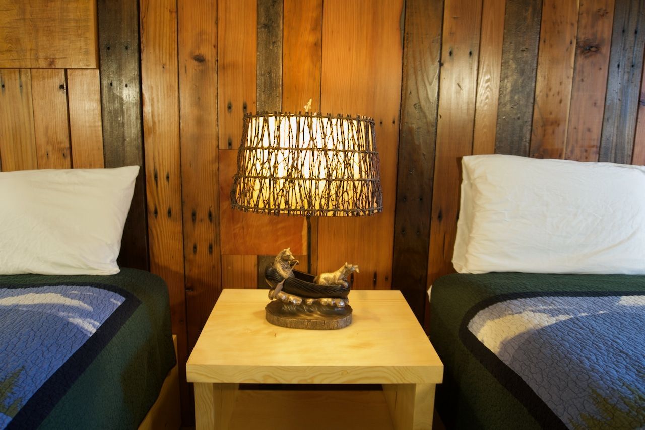 A bedroom with two beds and a lamp on a nightstand.