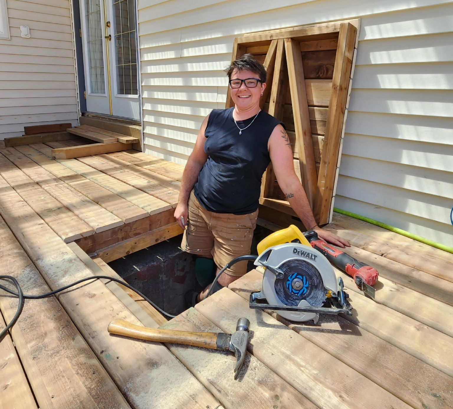 Person standing by a deck repair with tools and exposed joists beside a house