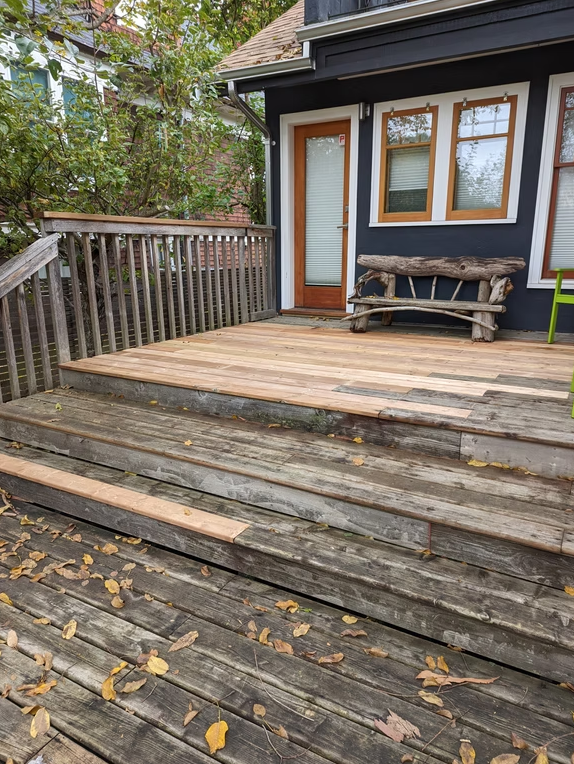 Weathered wooden deck with railing, steps, and a small house entrance with bench and windows