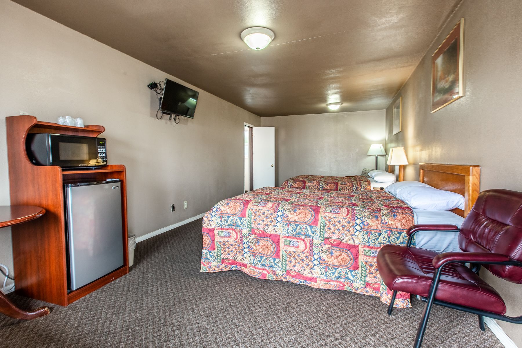 A hotel room with two beds , a chair , a microwave and a television.