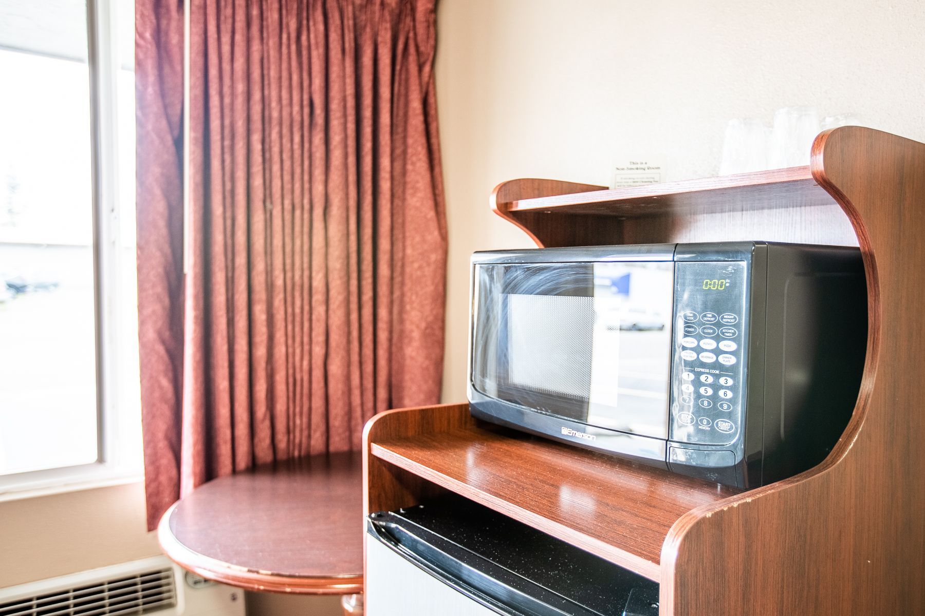 A microwave is sitting on top of a wooden shelf in a hotel room.