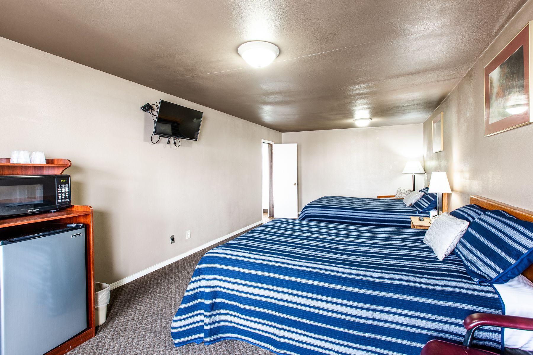 A hotel room with two beds , a microwave , and a refrigerator.