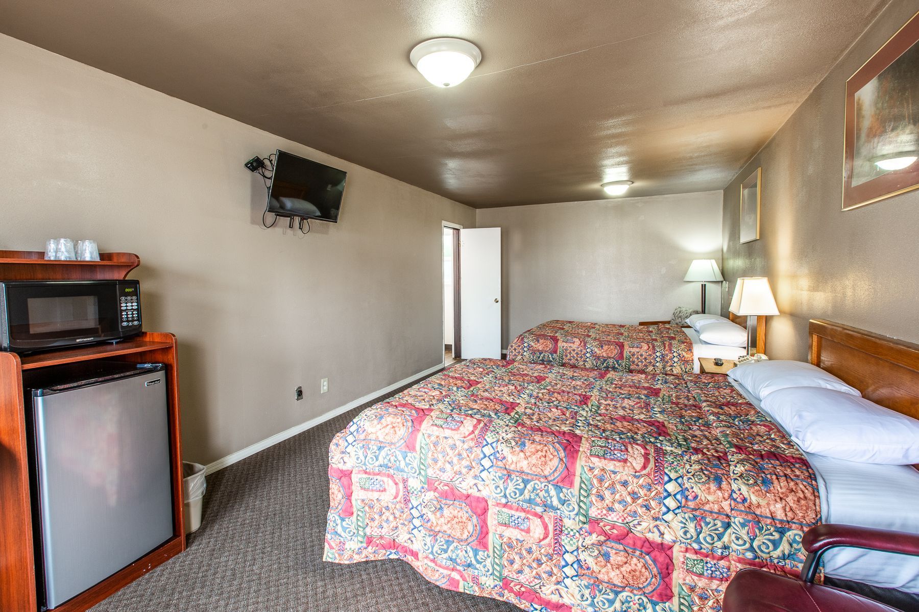A hotel room with two beds , a microwave and a refrigerator.