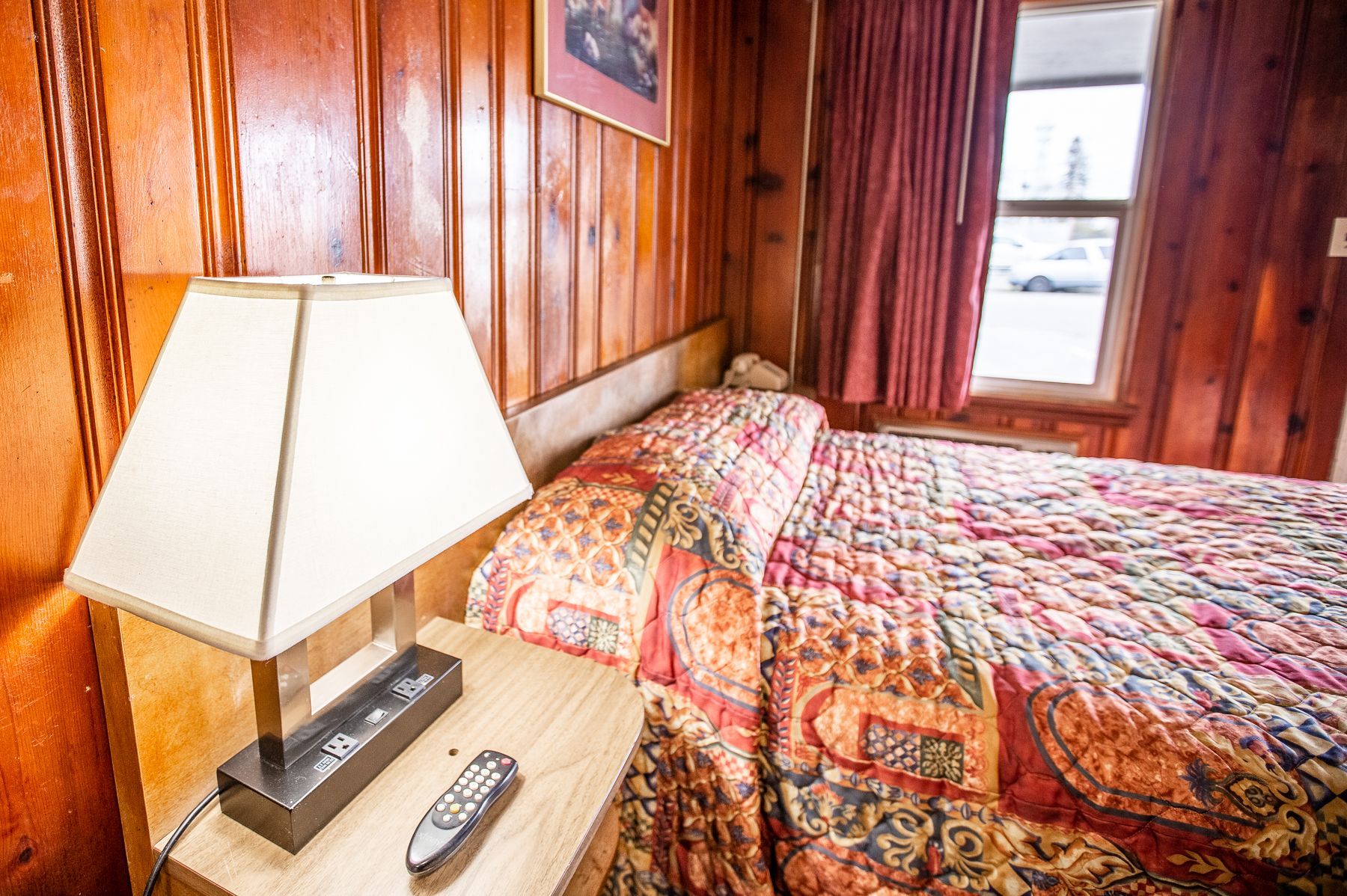 A bedroom with a bed , nightstand , lamp and remote control.