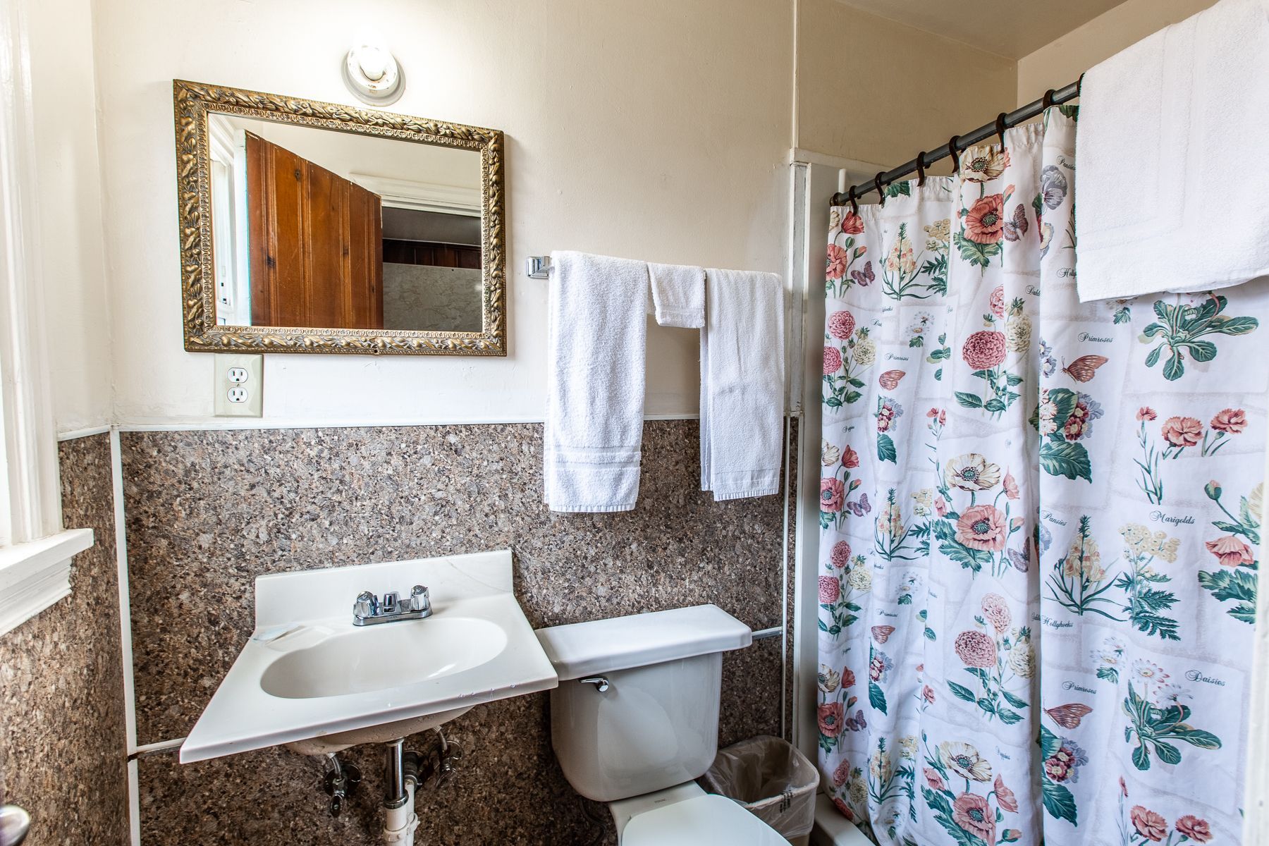 A bathroom with a toilet , sink , mirror and shower curtain.