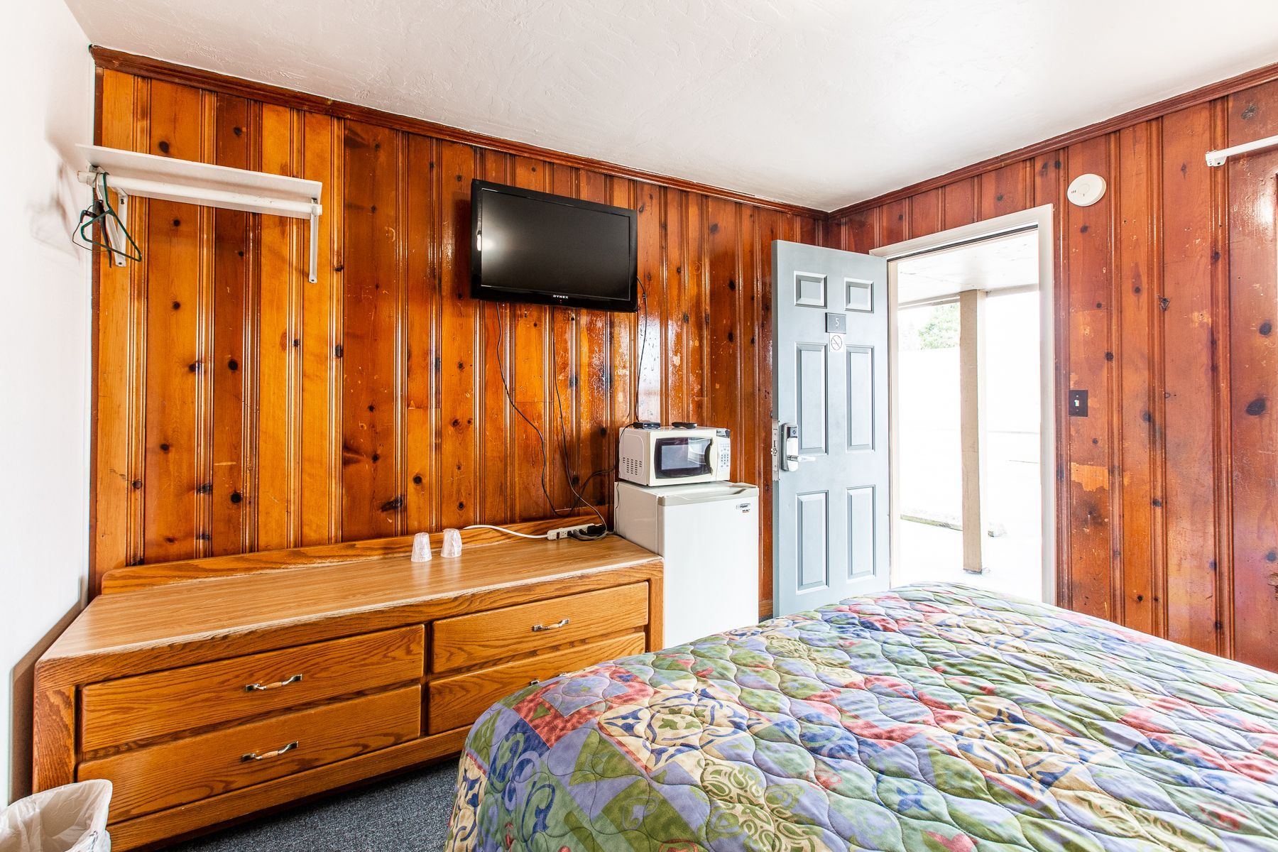 A hotel room with a bed , dresser , microwave and television.
