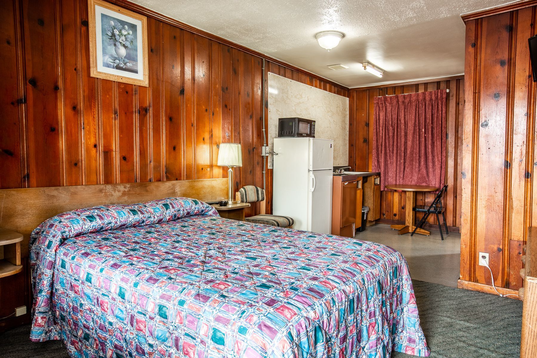 A hotel room with a bed , table , refrigerator and microwave.