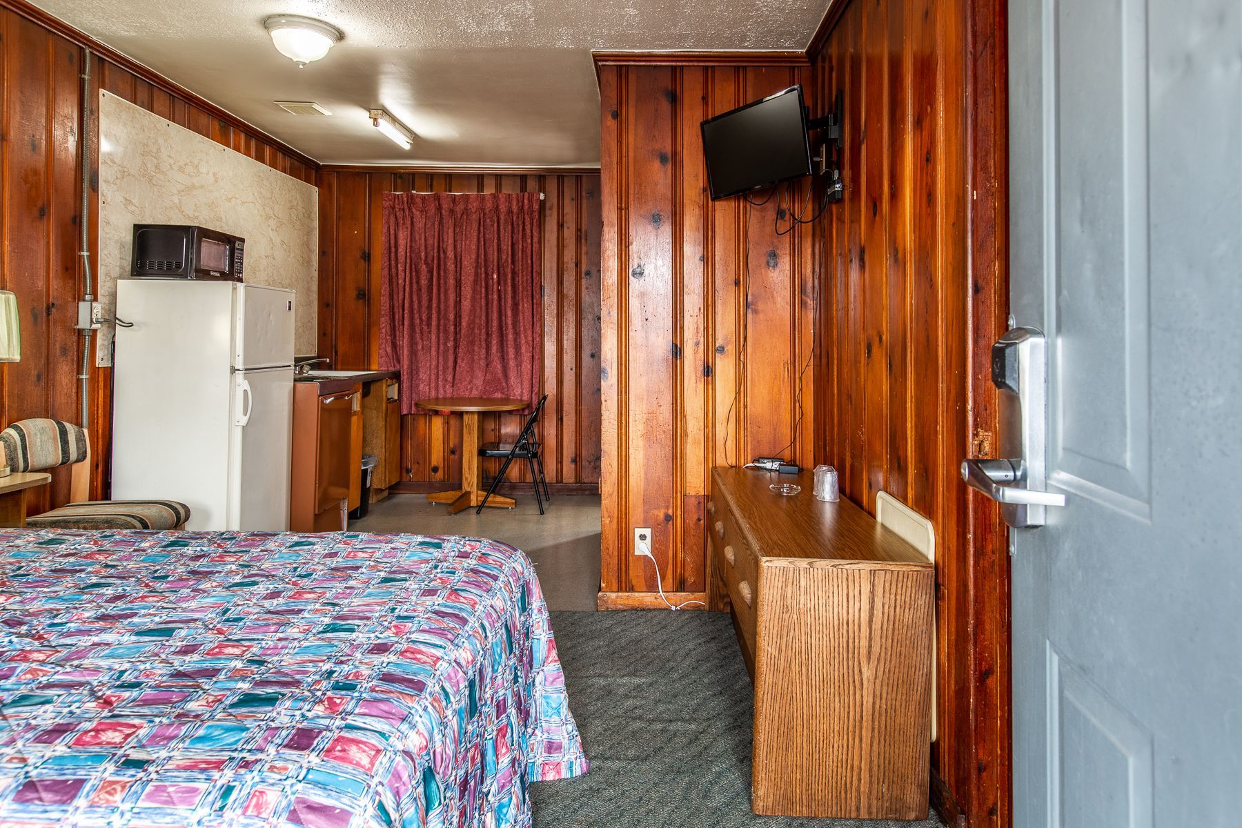 A hotel room with a bed , dresser , refrigerator and television.